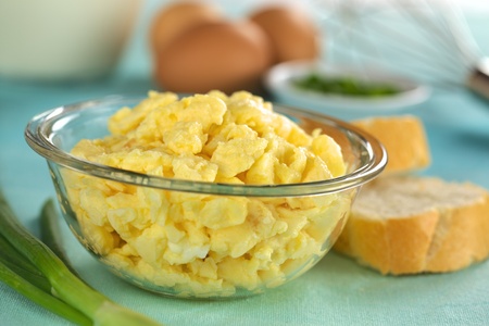 Scrambled eggs in glass bowl with baguette slices on the side and ingredients in the back (Selective Focus, Focus on the front of the scrambled eggs)の写真素材