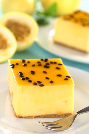 Fresh passion fruit cheesecake dessert on plate with pastry fork with another cake and yellow passion fruits in the back (Selective Focus, Focus on the left upper front edge of the cake)の写真素材