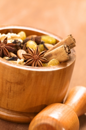 Baking ingredients such as star anise, clove, cinnamon, almond, raisin, sultana and walnut in wooden mortar with pestle in front (Selective Focus, Focus on the middle of the star anise in the front) の写真素材