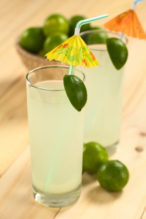 Freshly prepared refreshing lemonade out of limes in tall glass garnished with lime wedge and paper parasol (Selective Focus, Focus on the lime wedge)の写真素材