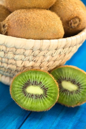 Half kiwi fruits on blue wood with kiwi fruits in basket behind (Selective Focus, Focus on the first half kiwi)の写真素材