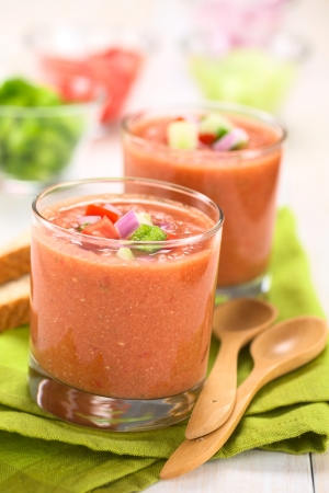 Traditional Spanish cold vegetable soup made of tomato, cucumber, bell pepper, onion, garlic and olive oil served in glasses (Selective Focus, Focus on the front of the vegetables on the top of the soup)の写真素材