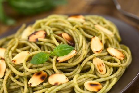Pasta with pesto made of basil and spinach garnished with roasted almonds served on a brown plate (Selective Focus, Focus on the basil leaf on the dish)  の写真素材