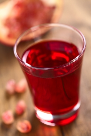 Grenadine syrup in shot glass with pomegranate seeds on the side and pomegranate in the back (Selective Focus, Focus on the front rim of the glass)の写真素材