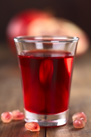 Grenadine syrup in shot glass with pomegranate seeds on the side and pomegranate in the back (Selective Focus, Focus on the front rim of the glass)の写真素材