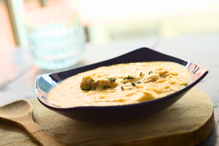 Thick yellow split pea soup with chicken and some oregano leaves on top served in blue soup plate on...