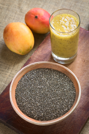Chia seeds (lat. Salvia hispanica) in clay bowl with mango and chia juice in the back photographed with natural light. Chia seeds are considered a superfood containing proteins, omega fats, minerals and antioxidants. (Selective Focus, Focus in the middle の写真素材