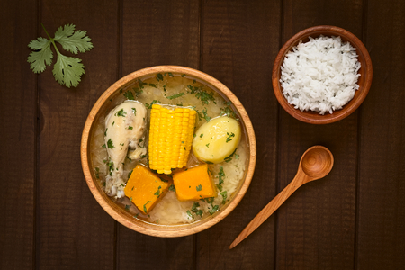 Overhead shot of traditional Chilean Cazuela de Pollo (or Cazuela de Ave) soup made of chicken, sweetcorn, pumpkin and potato, seasoned with fresh coriander served in wooden bowl and rice on the side の写真素材