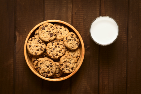 Overhead shot of chocolate chip cookies in wooden bowl with a glass of cold milk on the side photographed on wood with natural lightの写真素材