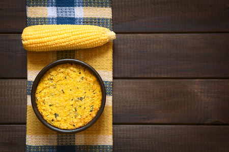 Overhead shot of traditional Chilean corn pie called Pastel de Choclo served in bowl, photographed on dark wood  with natural light. Below the corn-basil mix is ground meat, olive, boiled egg, raisins and pieces of chicken.の写真素材