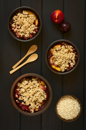 Overhead shot of rustic bowls filled with baked plum and nectarine crumble or crisp, photographed on dark wood with natural lightの写真素材
