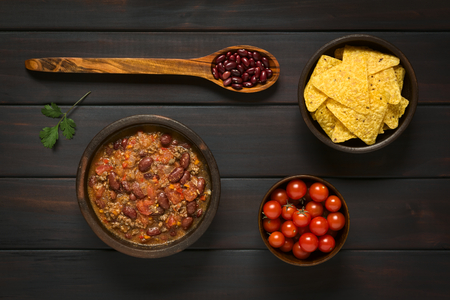 Overhead shot of chili con carne and tortilla chips with ingredients dried kidney beans and cherry tomatoesの写真素材