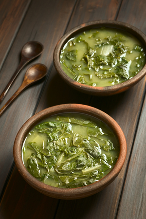 Two rustic bowls of chard soup with small wooden spoons on the side