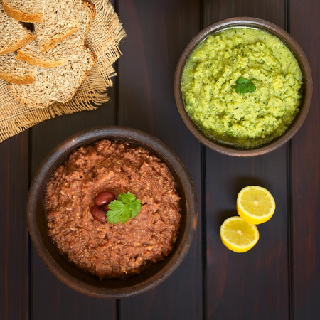 Overhead shot of rustic bowls of homemade vegetable spreads (red kidney bean, zucchini and parsley),...