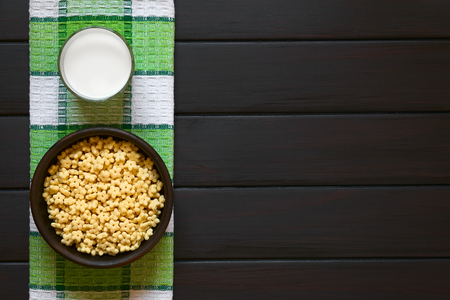 Honey flavored breakfast cereal in rustic bowl with a glass of milk, photographed overhead on dark wood with natural lightの写真素材