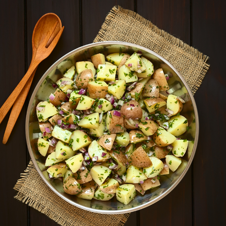Salad of jacket potato, red onion and herbs in bowl with wooden spoon and fork, photographed overhead on dark wood with natural lightの写真素材