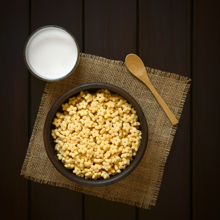 Honey flavored breakfast cereal in rustic bowl with a glass of milk and a wooden spoon on the side,...