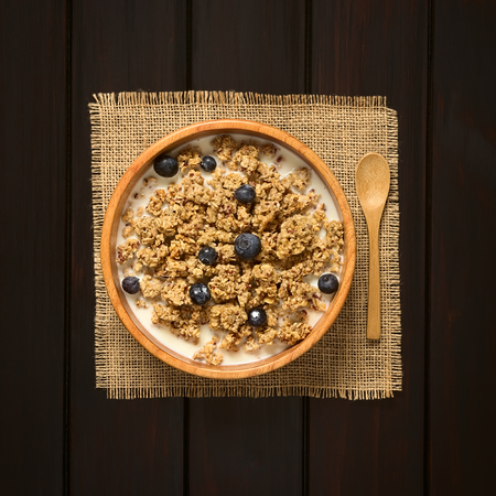 Dried berry and oatmeal breakfast cereal with fresh blueberries and milk in wooden bowl,...