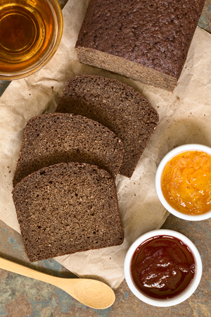 Slices of pumpernickel dark rye bread with strawberry and orange jam, cup of tea on the side,...