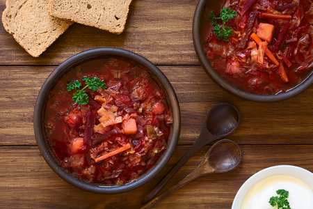 Vegetarian Borscht soup of Ukrainian origin made of beetroot, carrot, cabbage, potato, onion and celery in rustic bowls, with wholegrain bread and sour cream on the side, photographed overhead with natural light (Selective Focus, Focus on the soup)の写真素材