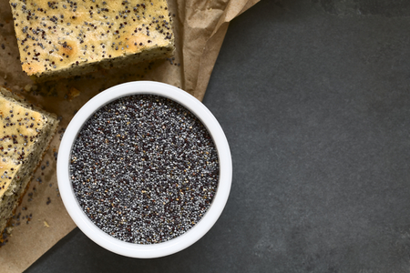 Poppy seeds in small bowl with poppy seed cake pieces on the side, photographed overhead on slate with natural lightの写真素材