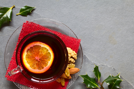 Mulled red wine with orange slice on top in glass cup, holly leaves on the side, photographed overhead on slate with natural light (Selective Focus, Focus on the mulled wine)の写真素材