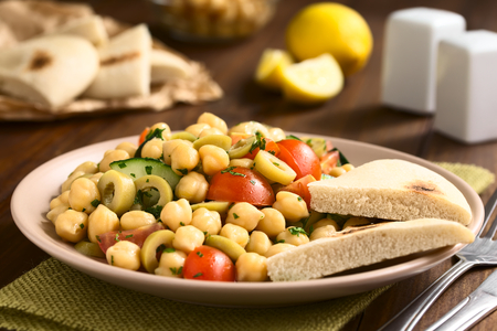 Chickpea salad with green olives, cucumber, cherry tomato and parsley, served on plate with pita bread pieces on the side, photographed with natural light (Selective Focus, Focus one third into the salad)の写真素材