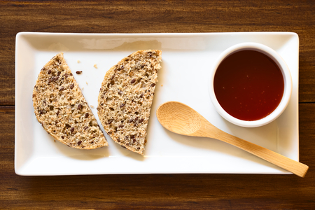 Homemade rose hip jam and wholegrain rolls on plate with small spoon, photographed overhead with natural lightの写真素材