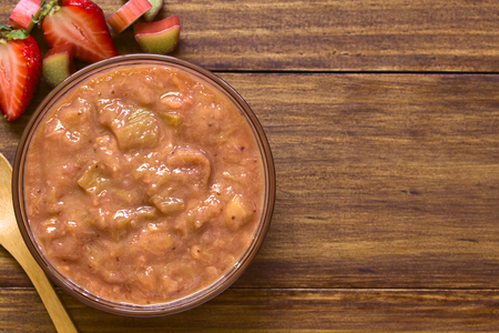 Homemade rhubarb and strawberry chutney in glass bowl, photographed overhead on dark wood with natural lightの写真素材