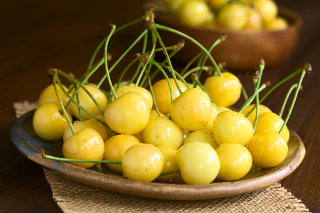 Ripe yellow or Rainier cherry on plate, photographed on wood with natural light (Selective Focus,...
