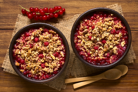Redcurrant crumble or crisp with oatmeal and walnut on top baked in rustic bowls, photographed overhead on dark wood with natural light (Selective Focus, Focus on the top of the crumbles)の写真素材