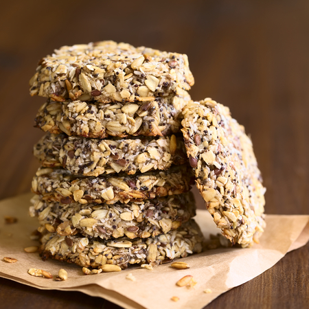 Vegan cookies made of banana, oatmeal and roasted oat grains, linseed, poppy seeds, grated coconut, chia seeds and cinnamon powder arranged in pile, photographed with natural light (Selective Focus, Focus on the front of the cookies)の写真素材