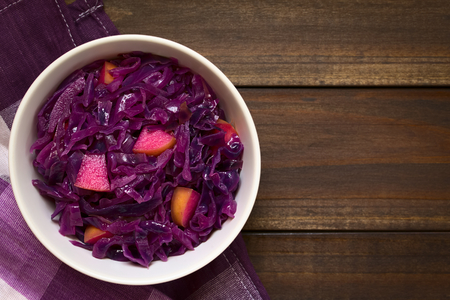 Braised red cabbage with apple in bowl, photographed overhead on dark wood with natural light (Selective Focus, Focus on the top of the dish)の写真素材