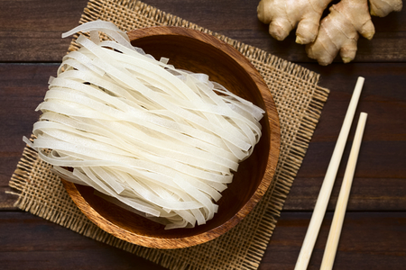 Raw rice flour noodles in wooden bowl, photographed overhead on dark wood with natural light (Selective Focus, Focus on the top of the noodles)の写真素材