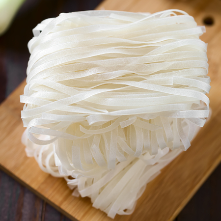 Raw rice flour noodle bundles piled on wooden board, photographed with natural light (Selective...