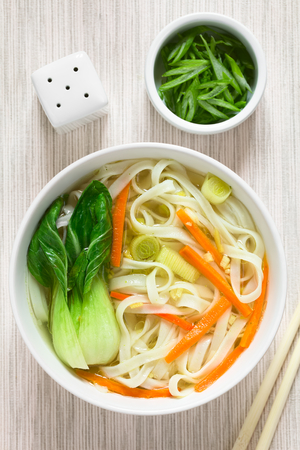 Vegetarian Asian rice noodle soup with bok choy, carrots and spring onion, photographed overhead...