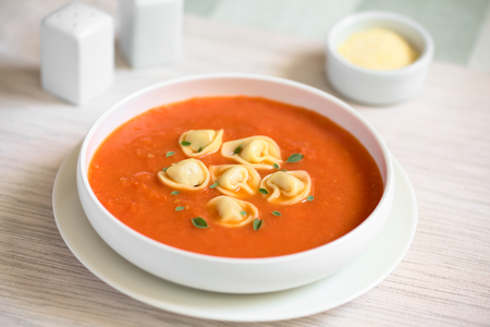 Homemade fresh cream of tomato soup with tortellini garnished with fresh oregano leaves, photographed with natural light (Selective Focus, Focus in the middle of the soup)の写真素材