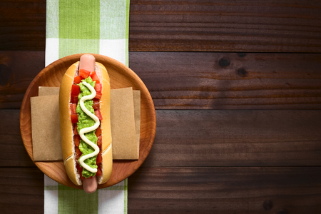 Chilean Completo Italiano (Italian) traditional hot dog sandwich, made of bread, sausage, tomato, avocado and mayonnaise, photographed overhead on dark wood with natural light (Selective Focus, Focus on the hot dog)の写真素材