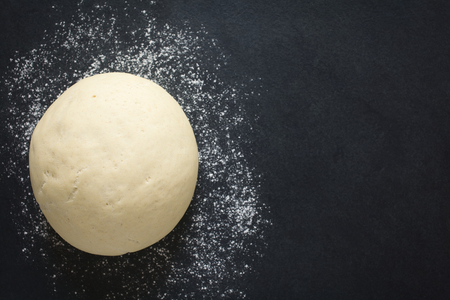 Risen or proved yeast dough for bread or pizza on a floured slate surface, photographed overhead with natural light (Selective Focus, Focus on the top of the dough)の写真素材