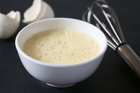 Whisked whole eggs (whites and yolks together) in bowl, with whisk and egg shells in the back, photographed on slate with natural light (Selective Focus, Focus one third into the whisked egg)の写真素材