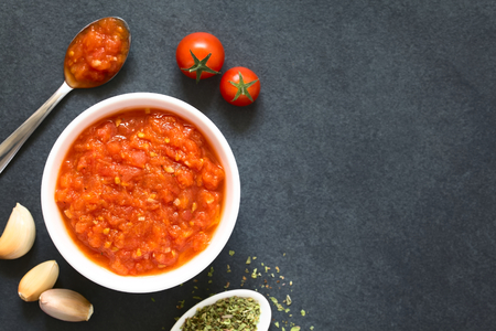 Homemade traditional Italian marinara or pomodoro tomato sauce made of fresh tomato, garlic, dried oregano and salt, served in bowl with ingredients on the side, photographed overhead on slate with natural light (Selective Focus, Focus on the top of the sの写真素材
