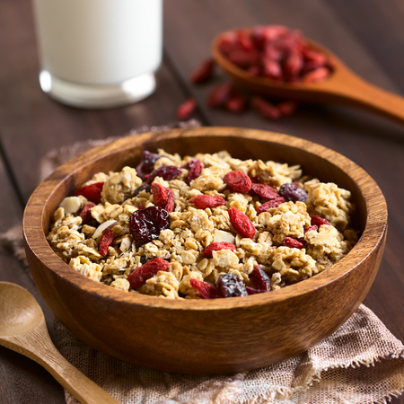 Crunchy oatmeal cereal with almond and dried goji berries and cranberries in wooden bowl, photographed with natural light (Selective Focus, Focus in the middle of the bowl)の写真素材