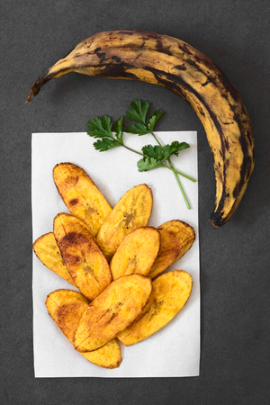 Fried slices of ripe plantains, a traditional and popular snack and accompaniment in Central America and Northern South America, photographed overhead on slate with natural lightの写真素材