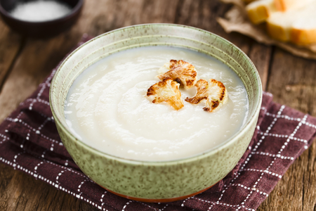 Fresh homemade cream of cauliflower soup garnished with roasted cauliflower floret slices (Selective Focus, Focus in the middle of the right floret on the soup)の写真素材
