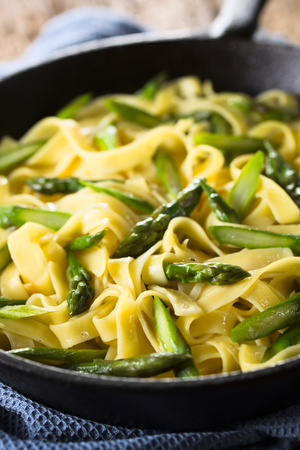 Fresh homemade pasta dish of fettuccine or tagliatelle, green asparagus, garlic and lemon juice in cast iron skillet (Selective Focus, Focus one third into the frying pan)の写真素材