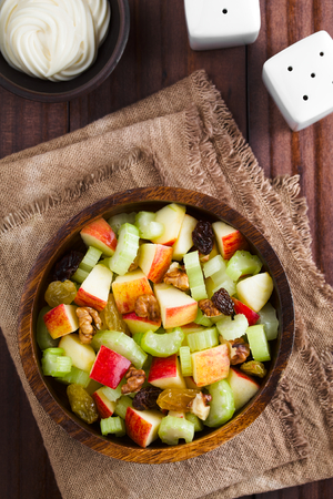 Fresh Waldorf salad made of celery, apple, walnuts, sultanas and raisins in wooden bowl with mayonnaise on the side, photographed overheadの写真素材