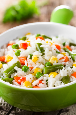 Cooked white rice mixed with colorful vegetables (onion, carrot, green peas, corn, green beans) in bowl (Selective Focus, Focus one third into the dish)の写真素材