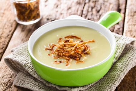 Fresh homemade cream of potato soup in green bowl garnished with crispy onion strings (Selective Focus, Focus one third into the bowl)の写真素材