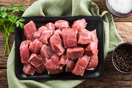 Fresh raw diced red beef meat on cast iron plate, fresh parsley, salt and pepper corns on the side, photographed overheadの写真素材