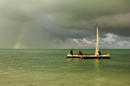 men on a pirogue, calm oily sea, rainbow and storm in the horizon